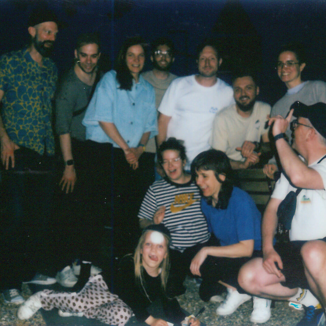 Gruppe von etwa zw&ouml;lf Menschen in verschiedenfarbiger Kleidung, die in einem Raum zusammensteht und sitzt, mit lockerer, freundlicher Atmosph&auml;re w&auml;hrend eines Gruppentreffens oder Workshops bei Studio Good in Berlin.