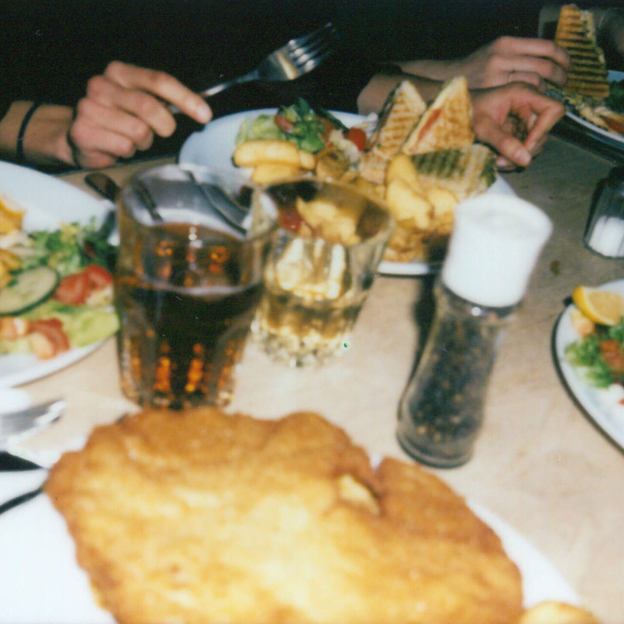 Tisch mit Tellern voller Fish and Chips, Pommes und anderen Speisen. H&auml;nde greifen nach Besteck und Gl&auml;sern mit Getr&auml;nken. Eine gesellige Mahlzeit mit Teamkollegen in einem Restaurant.