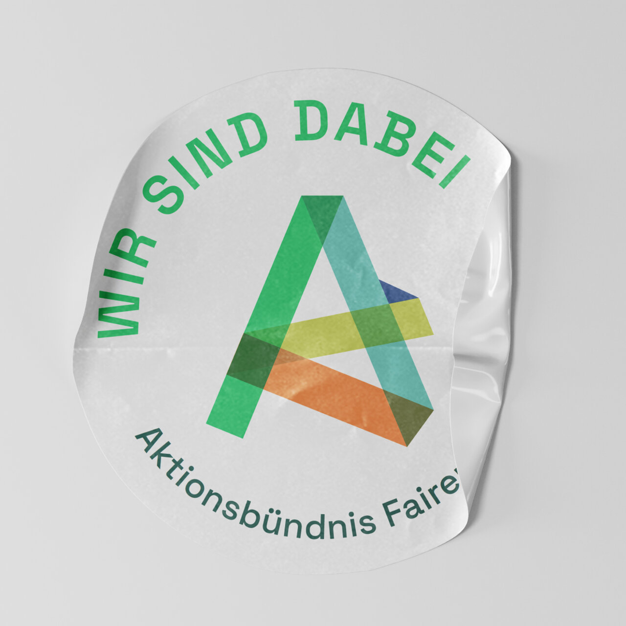 Rundes Aufkleber-Design mit dem Logo und Text "Wir sind dabei" der Aktionsb&uuml;ndnis Faire. Das Logo besteht aus &uuml;berlappenden, geometrischen Dreiecken in Gr&uuml;n-, Gelb-, Blau- und Oranget&ouml;nen, die ein abstraktes A-f&ouml;rmiges Symbol bilden.