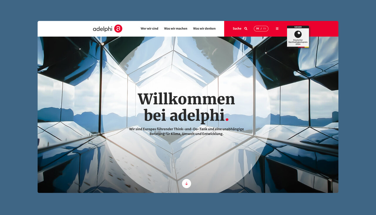 Symmetrische Spiegelung einer modernen Glasfassade mit Berglandschaft im Hintergrund, Startseite der Website von adelphi mit der Begr&uuml;&szlig;ung "Willkommen bei adelphi" in klarer, minimalistischer Typografie.