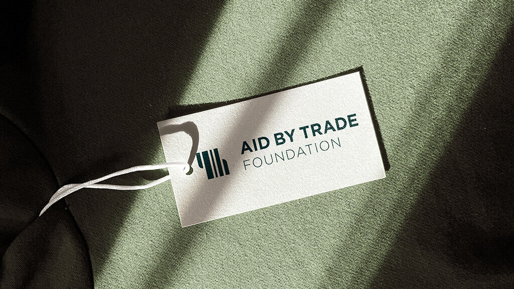 Etikett der Aid by Trade Foundation auf einem gewebten, gr&uuml;nen Hintergrund mit weichem Licht und Schatten.