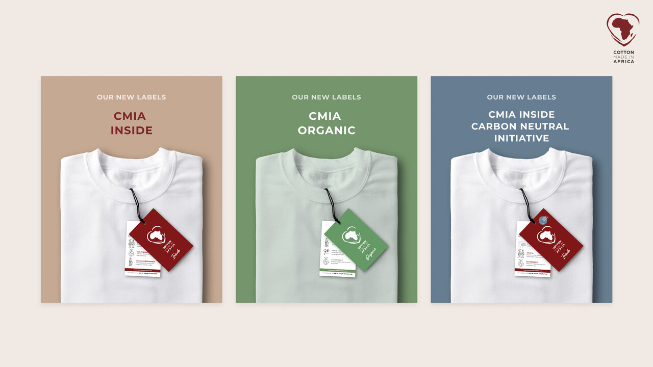 Drei CMIA-Hemden in verschiedenen Farbabstufungen - beige, gr&uuml;n und blau - pr&auml;sentiert mit einem roten Markenanh&auml;nger vor neutralem Hintergrund, die verschiedene Nachhaltigkeitslabels wie "Inside", "Organic" und "Carbon Neutral Initiative" zeigen.