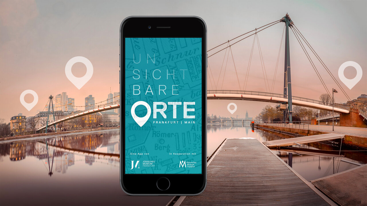 Smartphone mit der App &bdquo;Unsichtbare Orte" des J&uuml;dischen Museums Frankfurt vor einer Br&uuml;ckenlandschaft mit Spiegelung im Wasser, umrahmt von Geolocation-Markern.