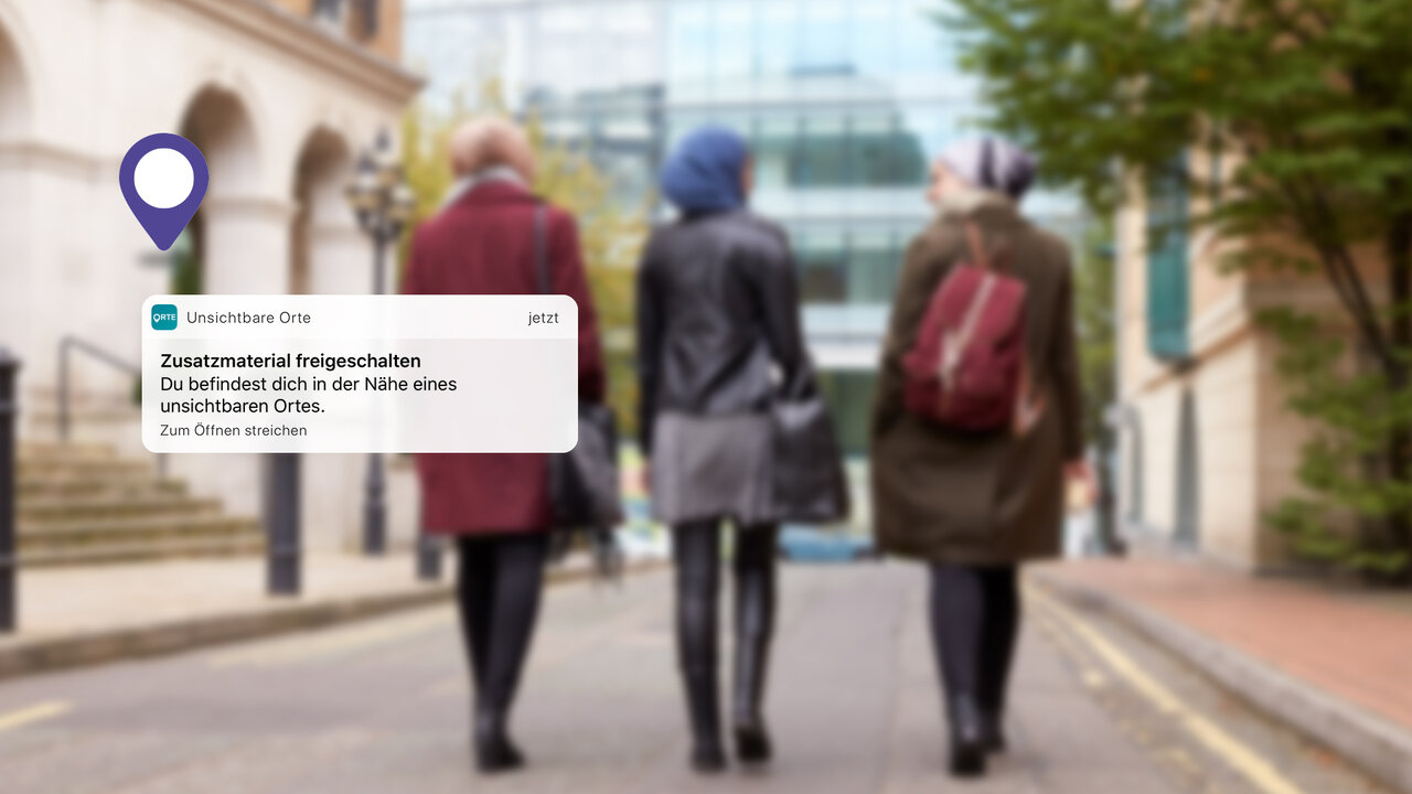Drei Personen von hinten auf einem Stadtstra&szlig;enabschnitt, von denen zwei eine Jacke in Rot und Gr&uuml;n und eine mit einem roten Rucksack tragen, mit einem Kartensymbol und einem Informationsoverlay im Design der App &bdquo;Unsichtbare Orte".