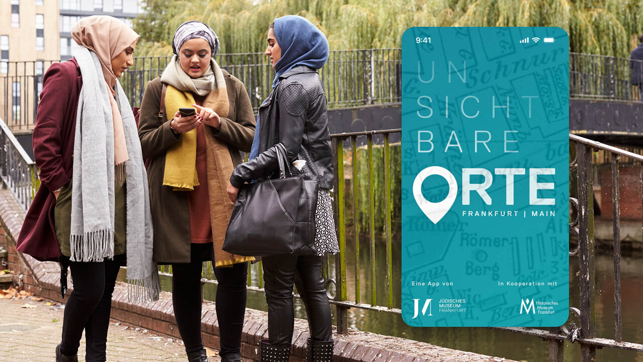 Drei Frauen mit Kopft&uuml;chern stehen an einem Gel&auml;nder, im Hintergrund ein Plakat f&uuml;r die App &bdquo;Unsichtbare Orte" des J&uuml;dischen Museums Frankfurt, das j&uuml;dische Zeitgeschichte und migrantische Geschichten im Stadtraum erkundet.