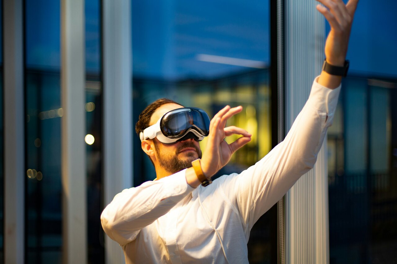 VR-Nutzer mit Headset in wei&szlig;em Langarmshirt gestikuliert expressiv vor einer Glasfassade, w&auml;hrend er eine virtuelle Erfahrung erkundet.