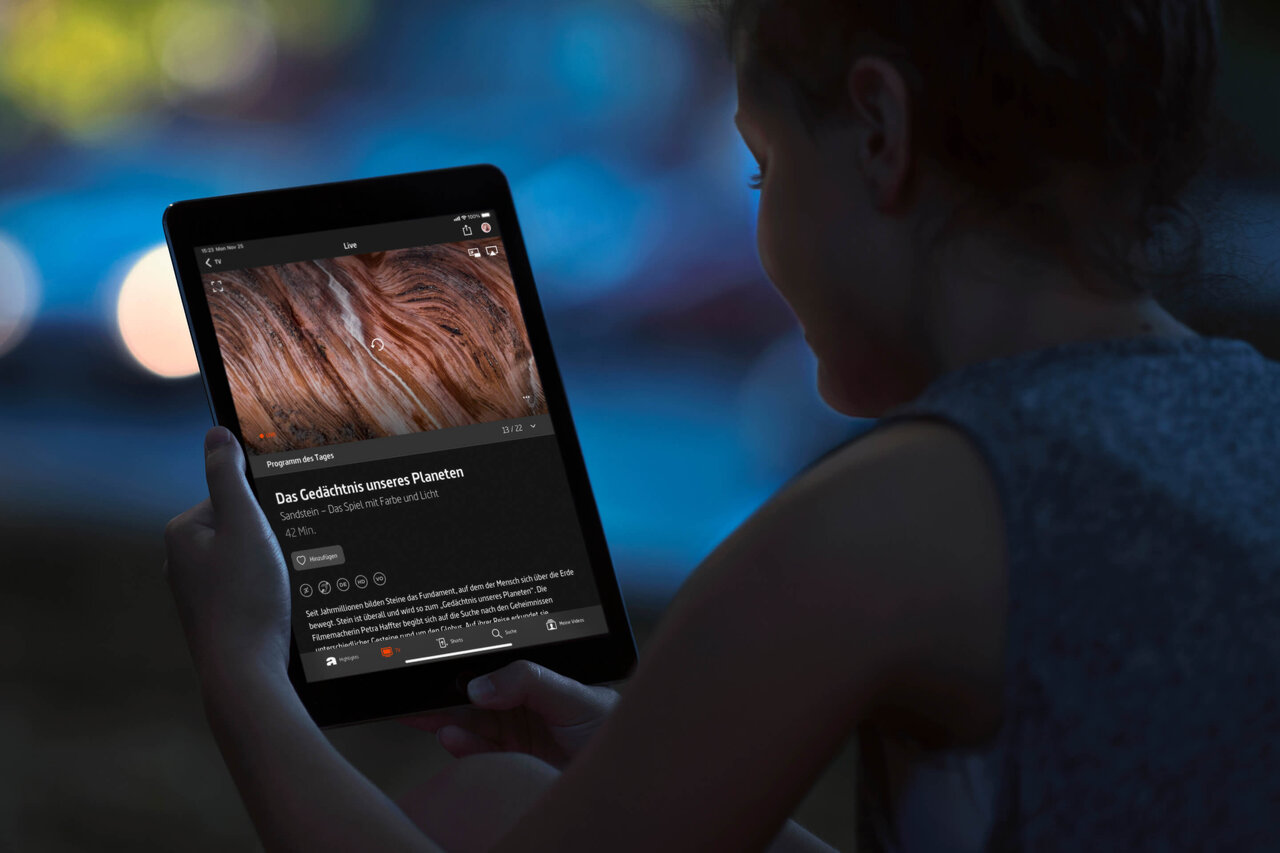 Eine Person schaut auf ein Tablet mit einer Webseite oder Anwendung, die eine detaillierte Nahaufnahme einer Textur oder Oberfl&auml;che zeigt, vor einem unscharfen blauen Hintergrund.