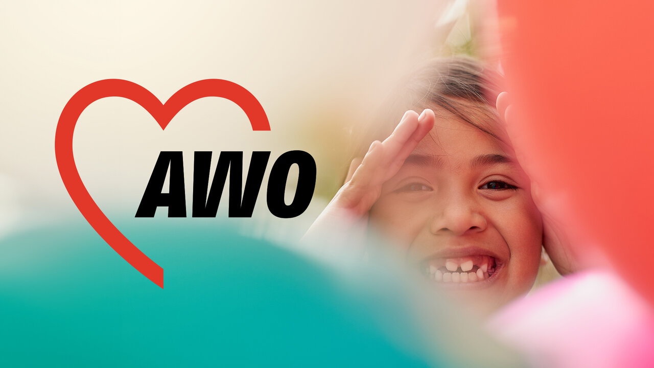 L&auml;chelndes Kind mit AWO-Logo in Herzform auf t&uuml;rkis-rosa Hintergrund, symbolisiert Vielfalt und soziales Engagement der Arbeiterwohlfahrt.