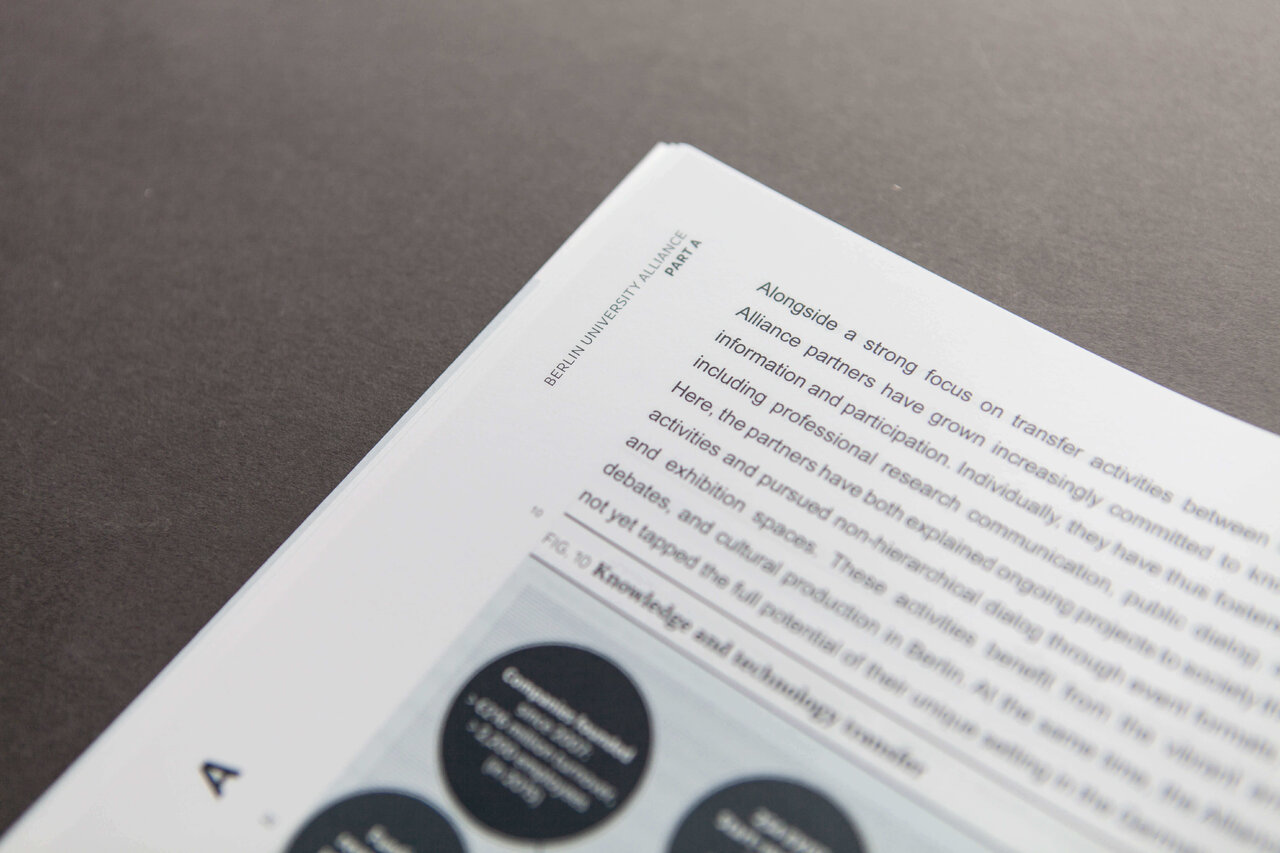Wei&szlig;es Papier mit Text und schwarzen Designelementen, leicht aus der Perspektive fotografiert vor einem grauen Hintergrund.