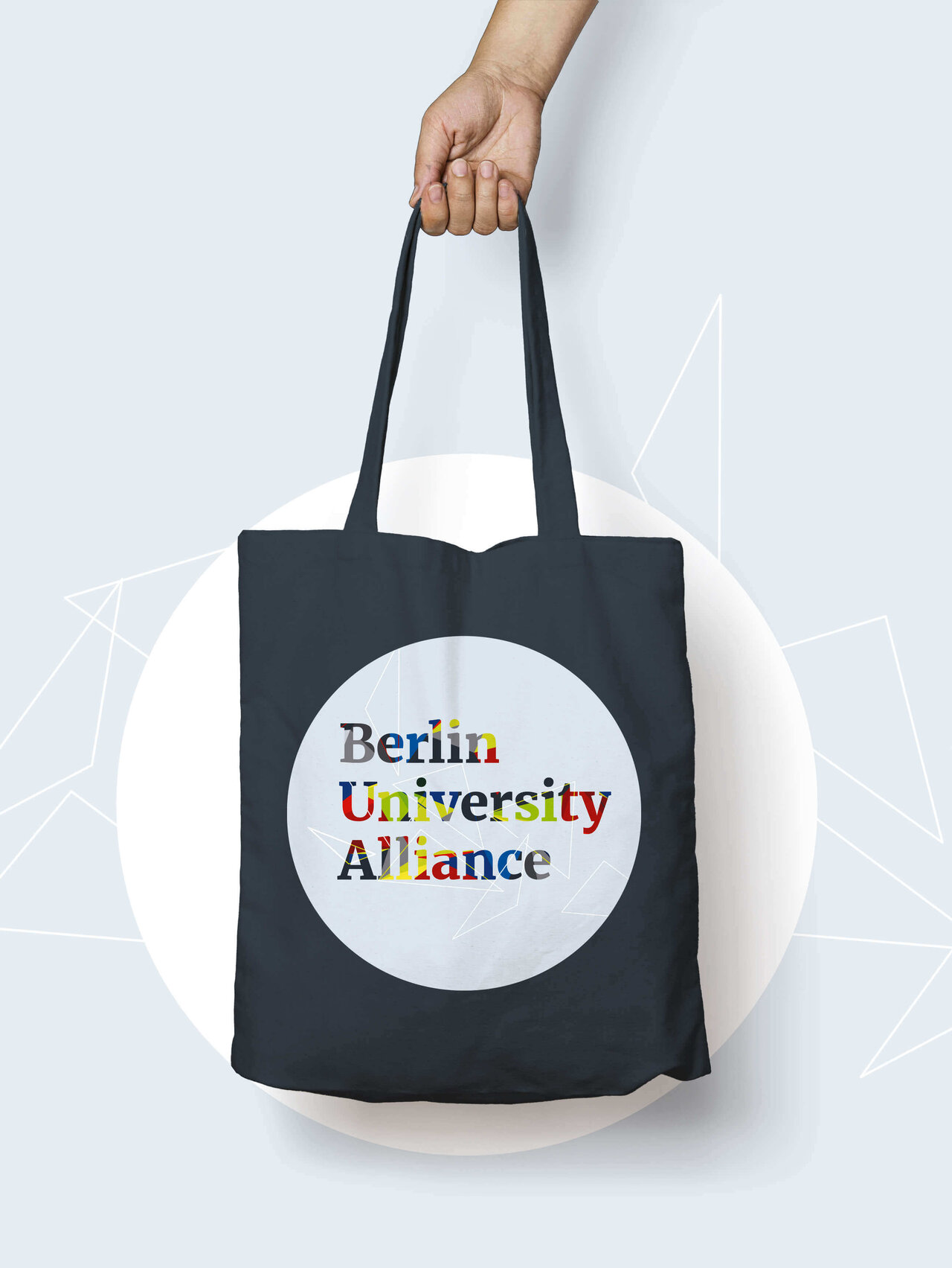 Schwarze Tasche mit dem Logo der Berlin University Alliance in wei&szlig;-bunten Buchstaben, pr&auml;sentiert von einer Hand, die den Tr&auml;ger hochhebt.