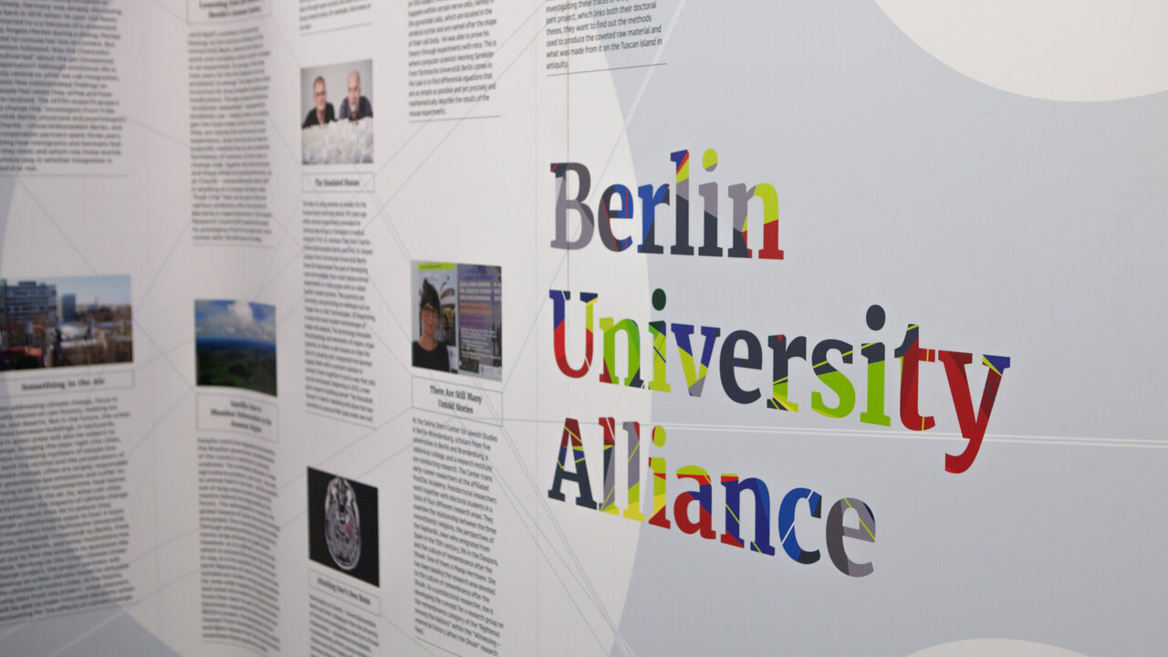 Farbenfrohe Schriftzug der Berlin University Alliance auf hellem Hintergrund mit Informationstafeln und Bildern, die eine Kooperation zwischen Berliner Universit&auml;ten und der Charit&eacute; dokumentieren.