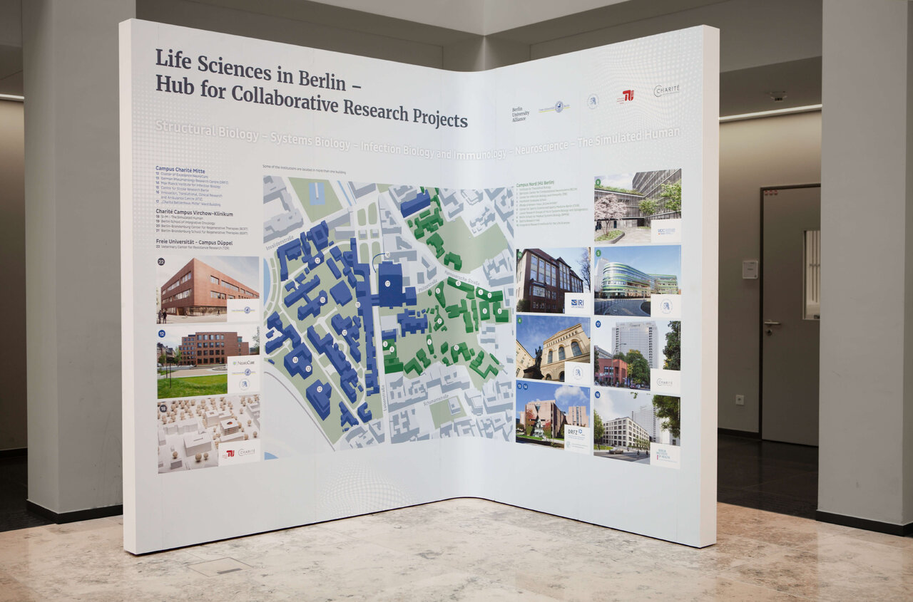 Ausstellungsstand mit einer Karte von Berlin und mehreren Fotos verschiedener Geb&auml;ude, der die Forschungsprojekte der Life Sciences in Berlin pr&auml;sentiert. Die Posterausstellung zeigt eine detaillierte &Uuml;bersicht des urbanen Gebiets mit farbcodierten Geb&auml;uden und Standortaufnahmen.
