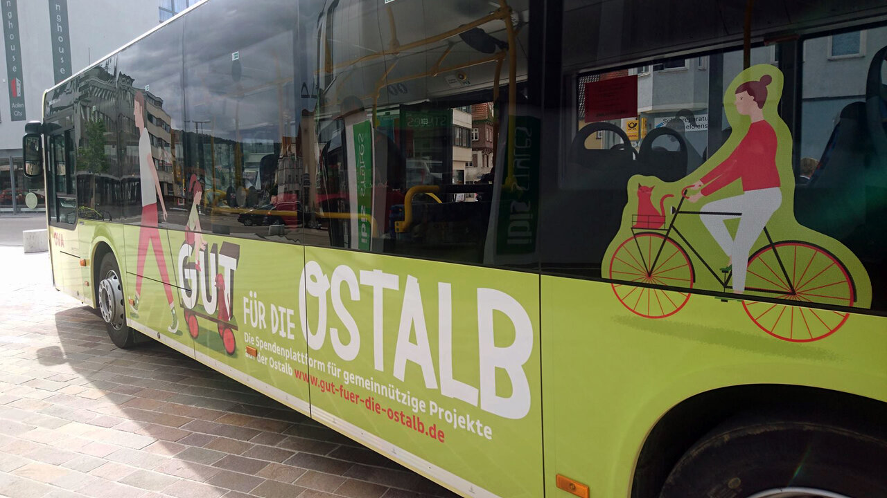 Gr&uuml;ner Stadtbus mit grafischer Darstellung eines Radfahrers, der Teil einer Kampagne zur F&ouml;rderung regionalen Engagements von betterplace.org und DSGV ist, mit auff&auml;lliger Gestaltung zur Aufmerksamkeitssteigerung f&uuml;r gemeinn&uuml;tzige Projekte.