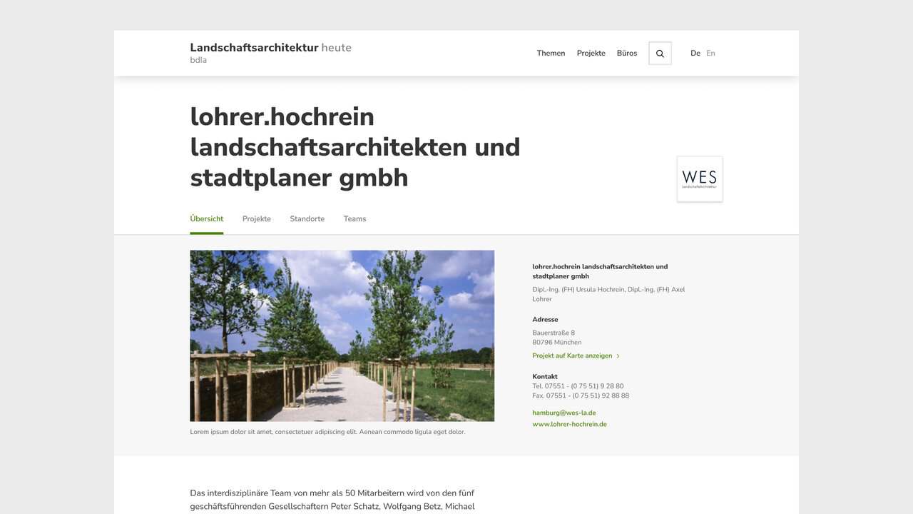 Ein gerader, von B&auml;umen ges&auml;umter Weg f&uuml;hrt durch eine gr&uuml;ne Landschaft, der durch Holzbarrieren begrenzt wird und eine ruhige, strukturierte Perspektive schafft.