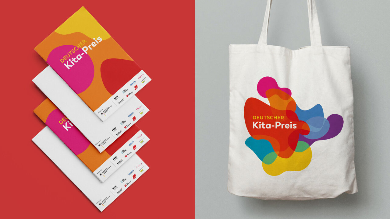 Gestaltung des Deutschen Kita-Preises mit buntem, abstraktem Logo auf wei&szlig;er Tasche und gestapelten Flyern vor rotem Hintergrund, die das visuelle Erscheinungsbild der Kampagne pr&auml;sentieren.