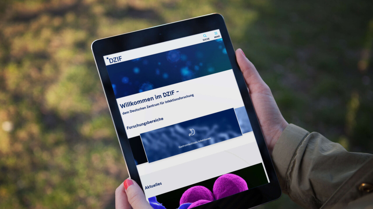 Eine Hand h&auml;lt ein Tablet mit der DZIF-Website vor einem unscharfen Hintergrund. Der Bildschirm zeigt die Startseite des Webportals mit dem DZIF-Logo und Navigationselementen.