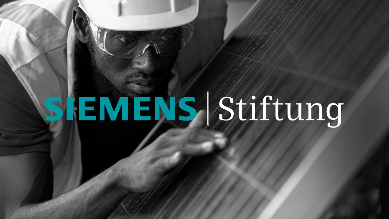 Ein Arbeiter mit Schutzhelm und Sonnenbrille arbeitet konzentriert an einem technischen Ger&auml;t oder einer Konstruktion, w&auml;hrend das Logo der Siemens Stiftung im Vordergrund steht.