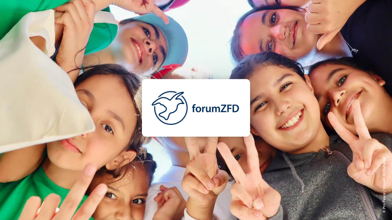 F&uuml;nf l&auml;chelnde junge Menschen bilden einen Kreis, blicken von oben in die Kamera und zeigen Friedenszeichen. Das Logo von forumZFD ist in der Mitte des Bildes platziert, symbolisch f&uuml;r Zusammenhalt und Friedensarbeit.