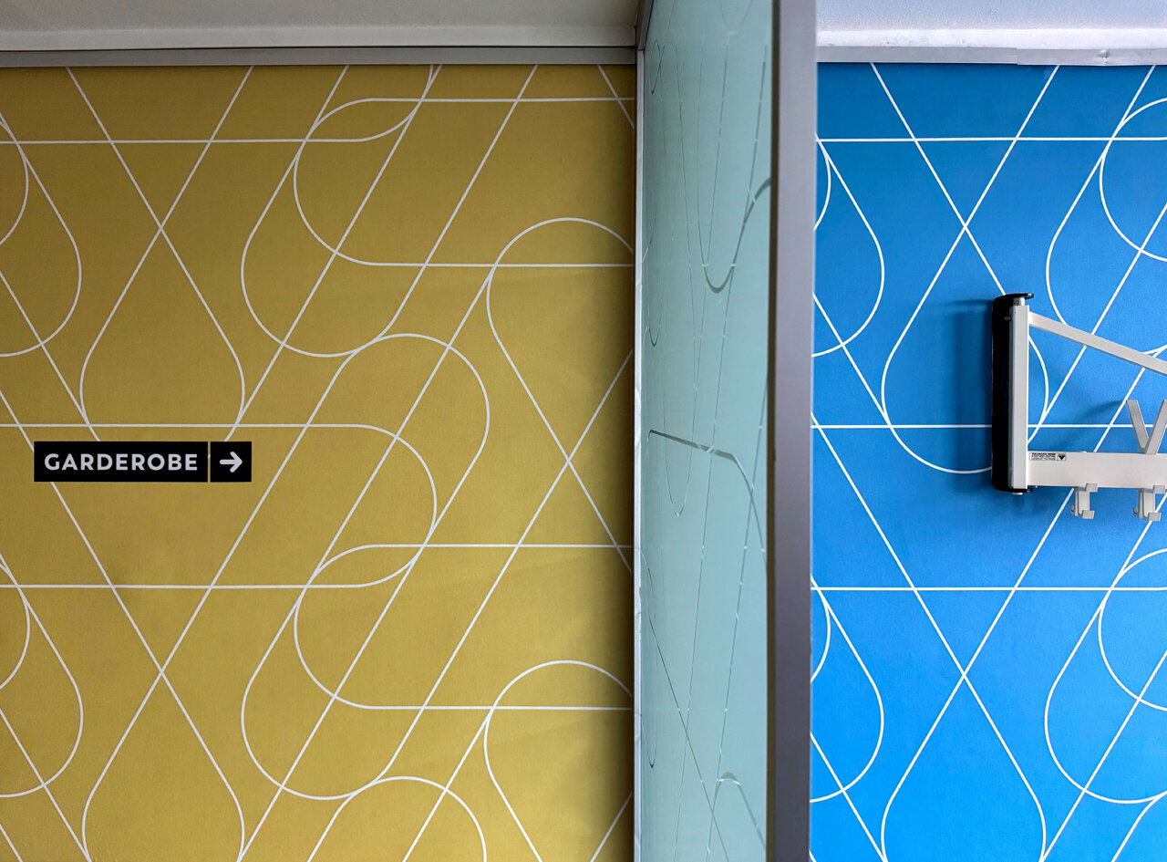 Gelbe und blaue Wand mit geschwungenen wei&szlig;en Linien, Garderobe-Schild und blauem Hintergrund mit Wandhalterung.