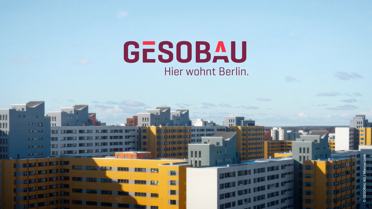 Blick auf Plattenbau-Wohnh&auml;user in Berlin mit dem Logo der GESOBAU, die bezahlbaren Wohnraum f&uuml;r Berliner B&uuml;rger bereitstellt. Die Geb&auml;ude sind in verschiedenen Grau- und Gelbt&ouml;nen gehalten und repr&auml;sentieren typische st&auml;dtische Architektur der Stadt.