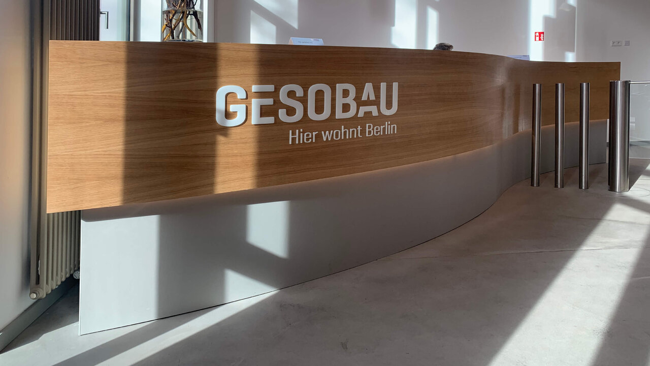 Curved Holzempfangstheke mit GESOBAU-Logo in wei&szlig;en Buchstaben, die den Eingangsbereich eines modernen B&uuml;rogeb&auml;udes in Berlin pr&auml;gen.