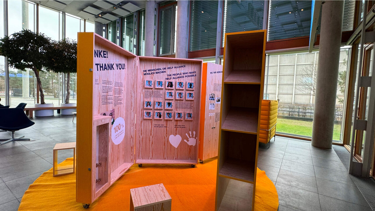 Ein kreatives Board mit dem Schriftzug "THANK YOU" in einem modernen B&uuml;roeingang, bestehend aus rosa-orangen Elementen und Regalen, die eine Collage von Bildern und Botschaften pr&auml;sentieren.