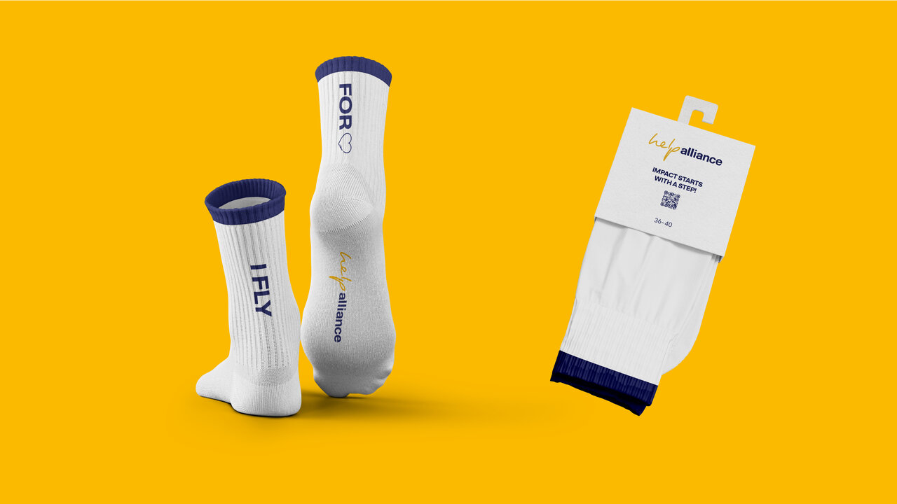 Drei wei&szlig;e Socken mit blau-wei&szlig;em Akzent vor leuchtendem gelbem Hintergrund, zwei aufrecht stehend und eine verpackt, mit dem Aufdruck "I FLY" auf den Socken.