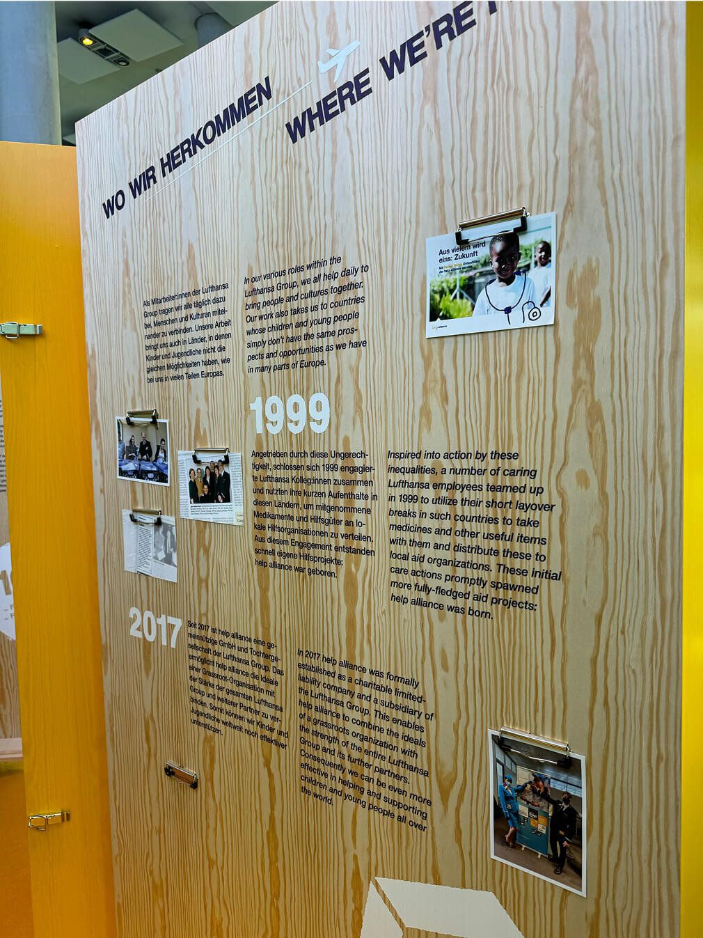Zeitreise-Wandtafel von Studio Good mit Holzhintergrund, die Meilensteine der Unternehmensgeschichte von 1999 bis 2017 dokumentiert, mit eingeklemmten Fotografien und Texten in deutscher Sprache, die die Entwicklung und Projekte des Unternehmens beschreiben.