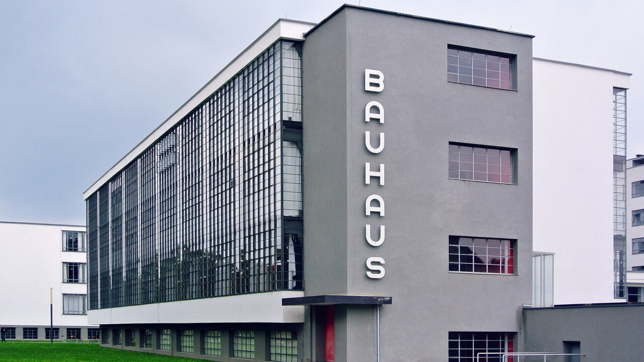 Bauhaus-Geb&auml;ude in Dessau, entworfen von Walter Gropius. Markantes Beispiel der Moderne mit Glasfassade, kubischer Architektur und vertikaler Beschriftung "BAUHAUS" an der Fassade. Charakteristisches Geb&auml;ude der Architekturgeschichte mit klaren Linien und funktionaler Gestaltung.