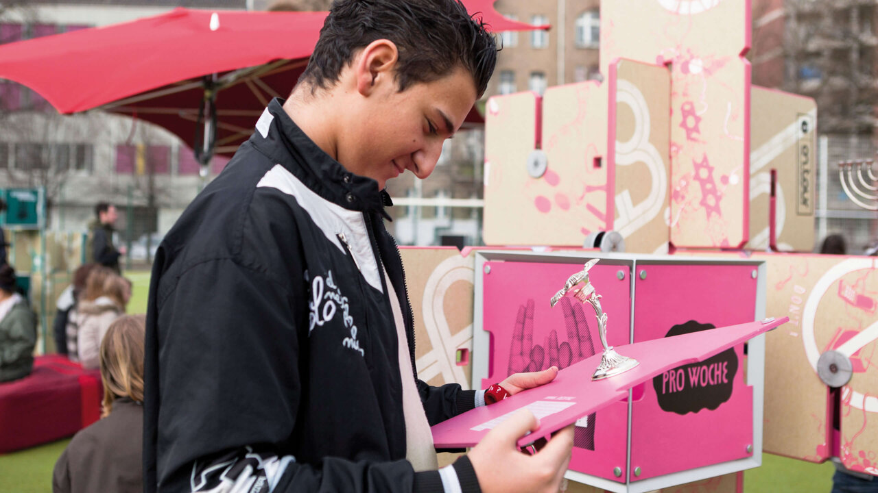 Eine Person in schwarzer Jacke bedient eine interaktive Station mit pinken Elementen, Teil der mobilen Ausstellung des J&uuml;dischen Museums Berlin zur F&ouml;rderung von Dialog und Verst&auml;ndnis.
