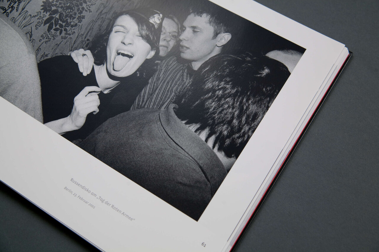 Eine schwarzwei&szlig;e Fotografie in einem ge&ouml;ffneten Buch, die zwei Personen in dichter N&auml;he zeigt, wobei eine Person laut lachend mit offenem Mund dargestellt ist und die andere Person daneben ruhig sitzt.