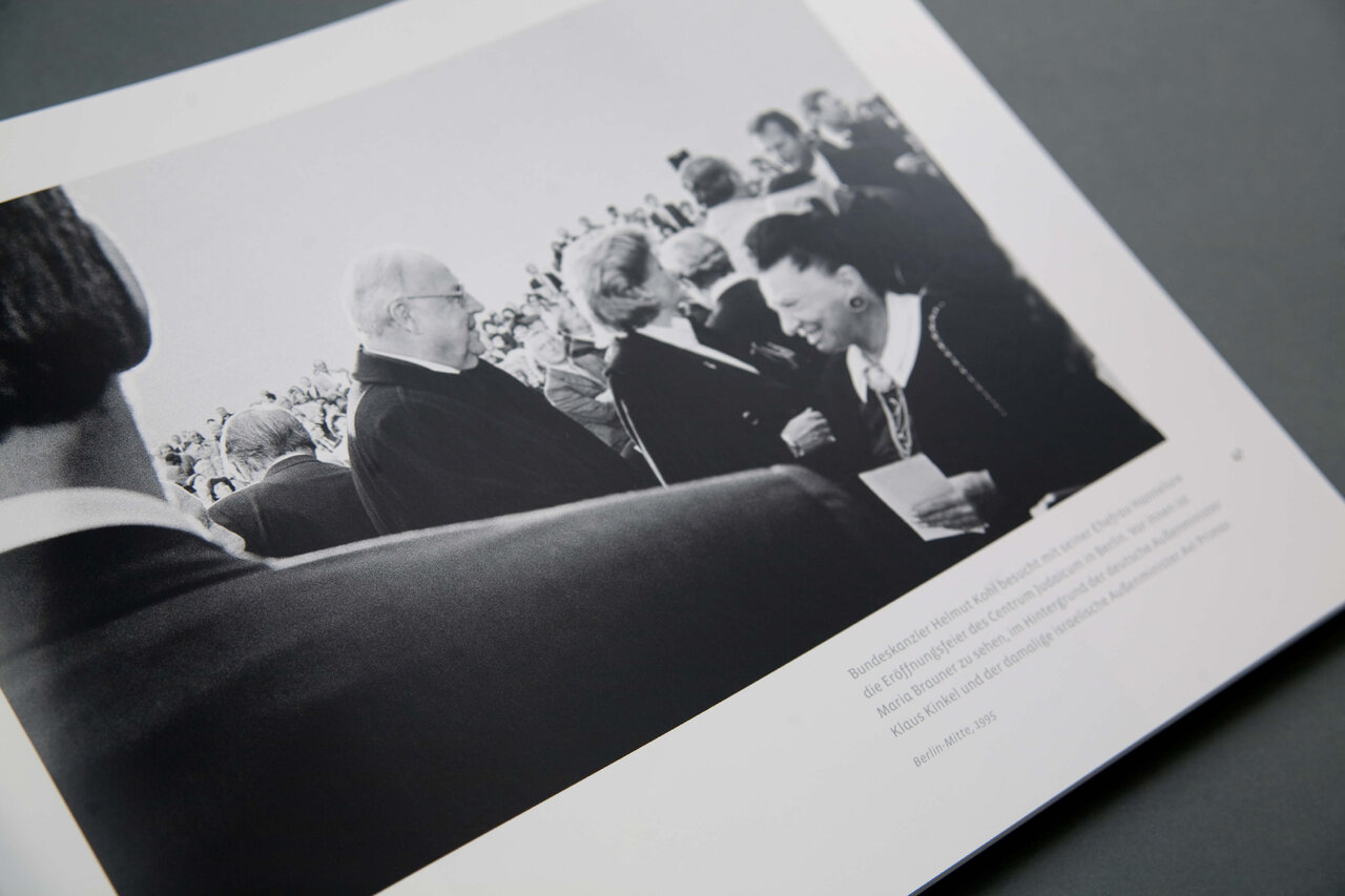 Schwarzwei&szlig;fotografie einer Gruppe von Menschen in einem Besprechungsraum, die in eine Diskussion vertieft sind, mit mehreren Personen, die an einem Tisch sitzen und sich austauschen.