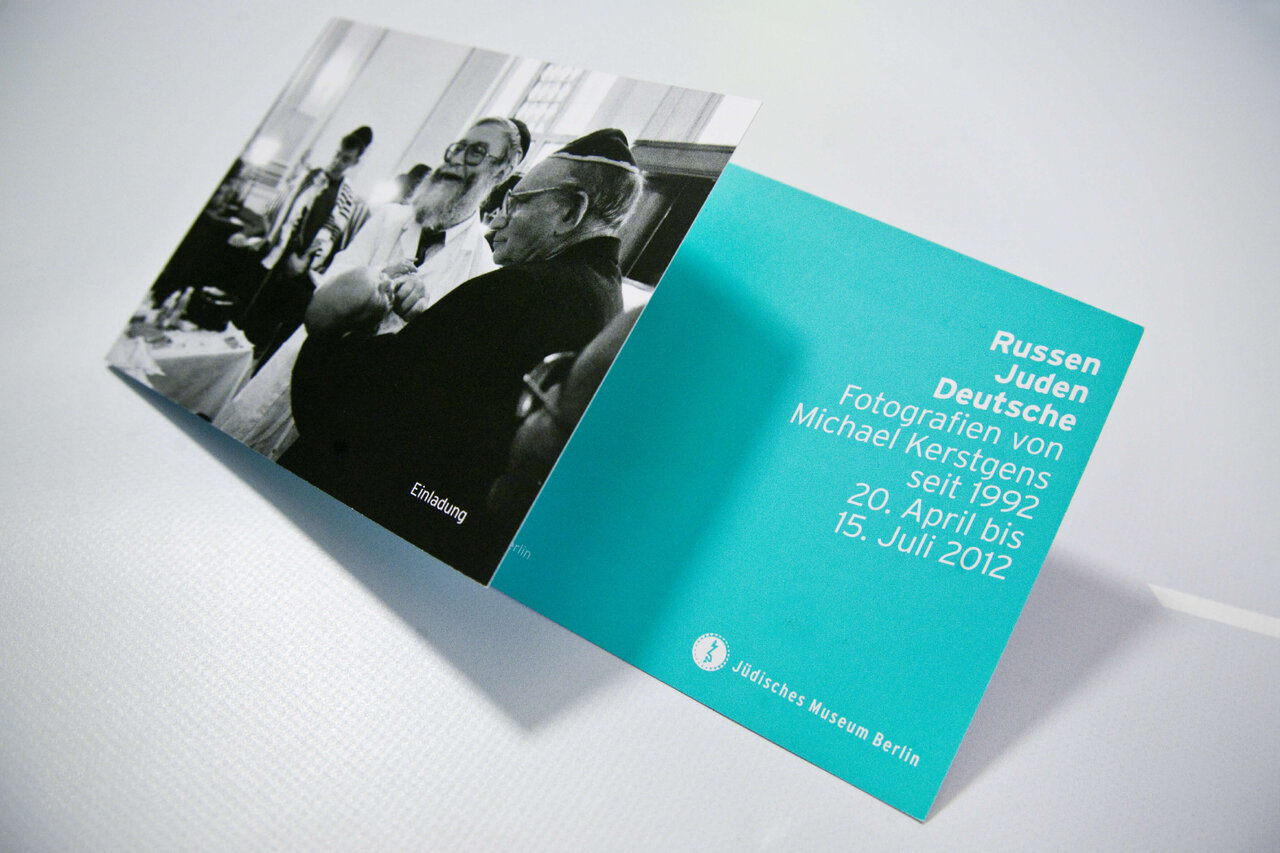 Aufgeschlagene Ausstellungsbrosch&uuml;re mit schwarzwei&szlig;em Foto und t&uuml;rkisfarbener Titelseite f&uuml;r die Publikation "Russen Juden Deutsche" von Michael Kerstgens, die j&uuml;disches Leben in Deutschland dokumentiert.