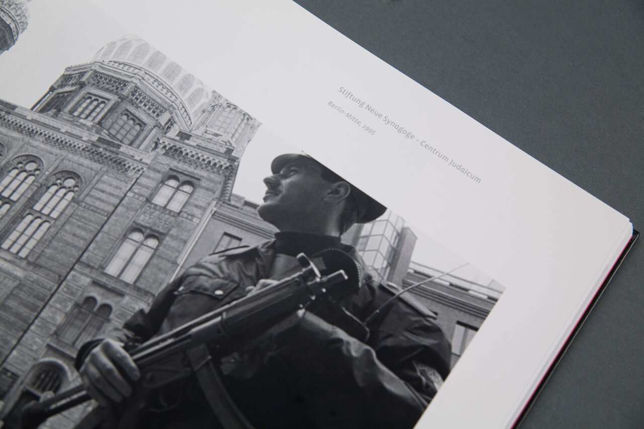 Schwarzwei&szlig;fotografie eines Soldaten mit Gewehr vor einem historischen Geb&auml;ude, der aufmerksam und konzentriert in einer markanten Pose steht.