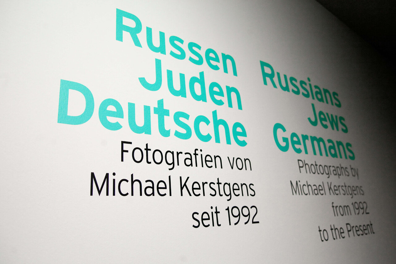 Ausstellungsplakat f&uuml;r Michael Kerstgens' Fotografie-Projekt "Russen Juden Deutsche" in t&uuml;rkiser Schrift, dokumentiert j&uuml;disches Leben in Deutschland seit 1992.