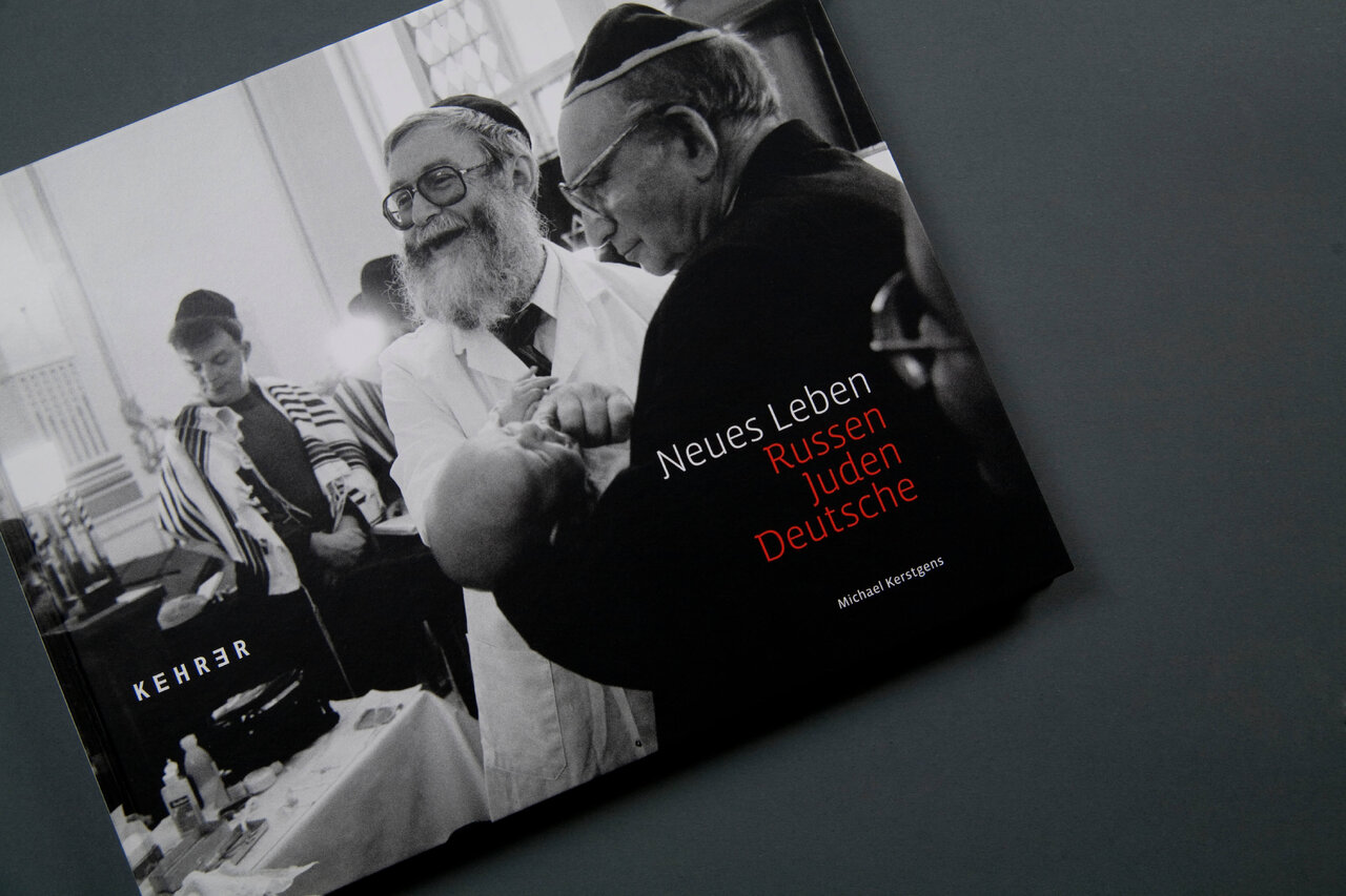 Zwei Buchumschl&auml;ge des Projekts "Neues Leben, Russen Juden Deutsche" von Michael Kerstgens, ein Schwarzwei&szlig;foto mit Menschen im Hintergrund, pr&auml;sentiert auf einer grauen Oberfl&auml;che.