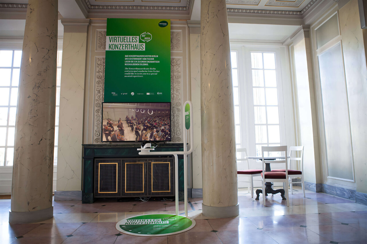 Eine Museumsinstallation mit gr&uuml;nem Informationsschild, historischem Holzschrank und wei&szlig;en S&auml;ulen, die einen Ausstellungsraum mit nat&uuml;rlichem Licht und minimalistischem Design pr&auml;sentieren.