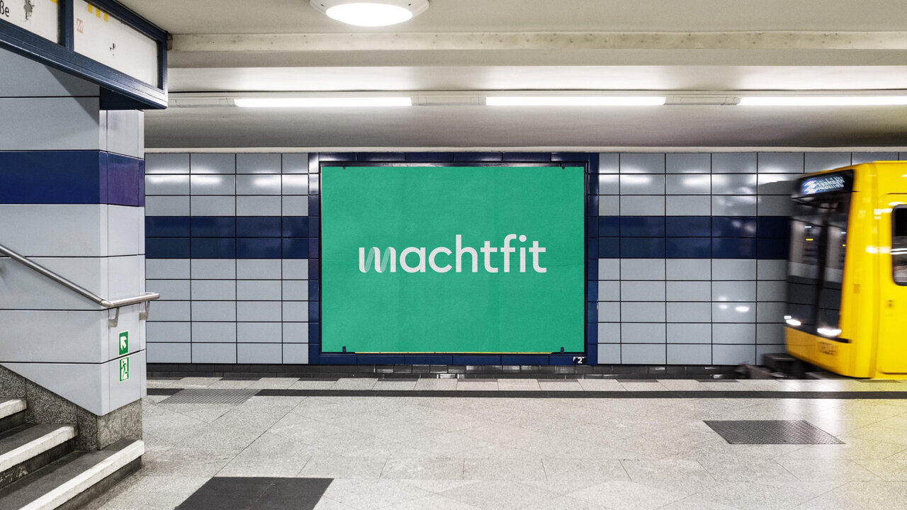 Machtfit-Werbeplakat in gr&uuml;ner Farbe an einer grauen U-Bahn-Station, mit einer gelben U-Bahn, die im Hintergrund vorbeif&auml;hrt.