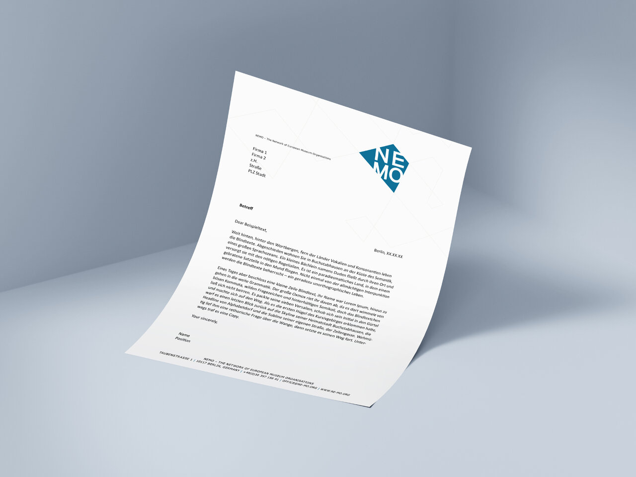 Briefpapier von Studio Good mit dem blauen NEMO-Logo, pr&auml;sentiert auf einem neutralen grauen Hintergrund, das die Gestaltung eines professionellen Dokuments f&uuml;r das Netzwerk Europ&auml;ischer Museumsorganisationen zeigt.