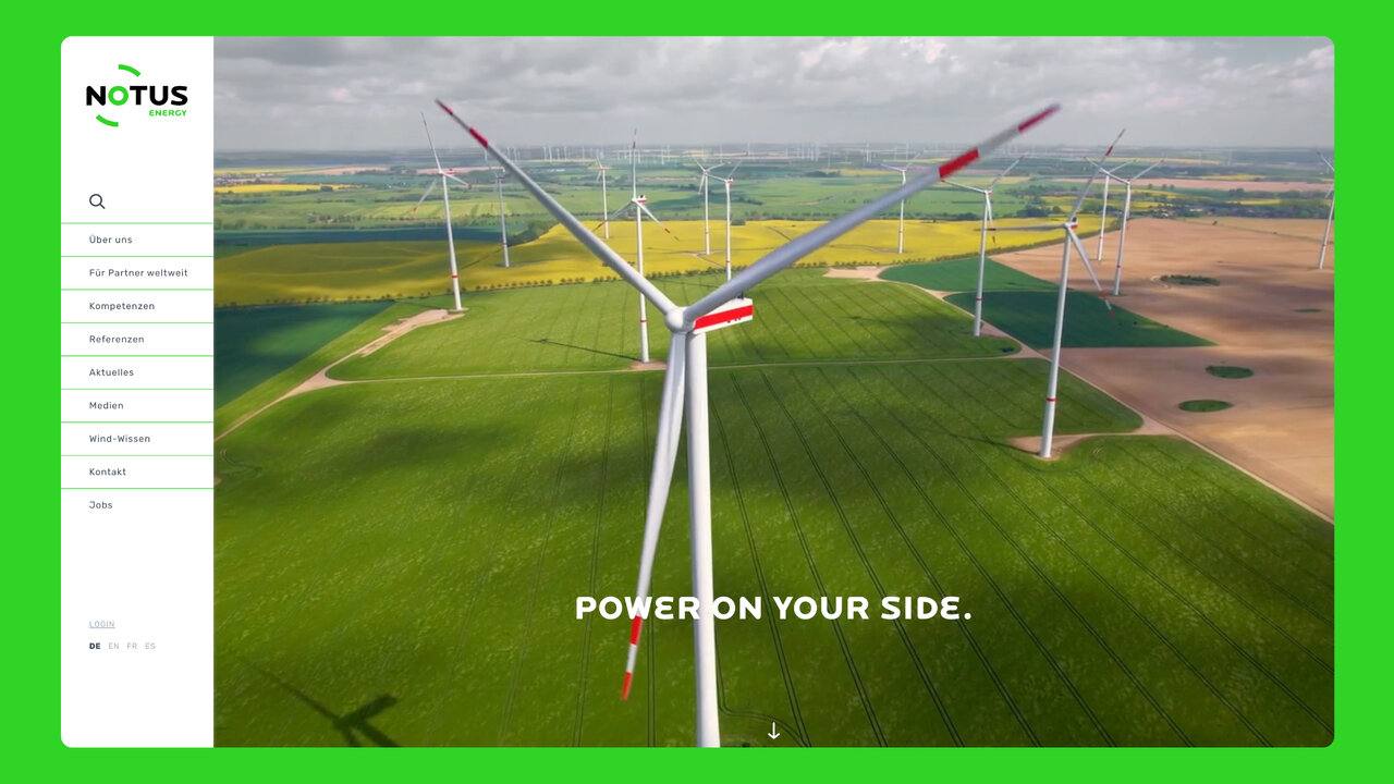Luftaufnahme eines Windparks mit mehreren Windturbinen auf gr&uuml;nen Feldern, die erneuerbare Energietechnologie und Nachhaltigkeit symbolisieren. Die Windr&auml;der sind wei&szlig; und rot und erstrecken sich &uuml;ber eine weite landwirtschaftliche Landschaft.