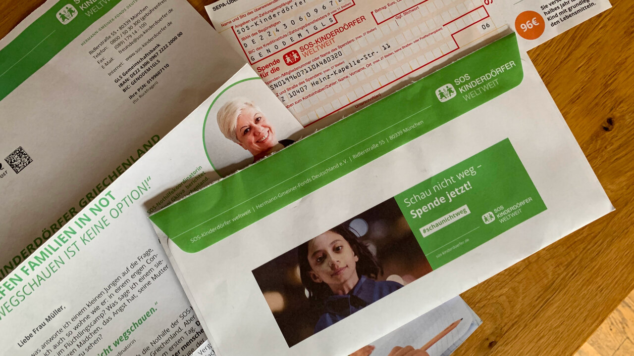Mehrere Briefdokumente, die Spender und Spenderinnen der SOS Kinderd&ouml;rfer weltwelt erhalten. Auf einem der Umschl&auml;ge ist das Kampagnenmotiv der Schau-nicht-weg-Kampagne zu sehen. Ein Kind, welches ernst in die Kamera blickt ist zu sehen neben einer gr&uuml;nen Fl&auml;che mit Text.