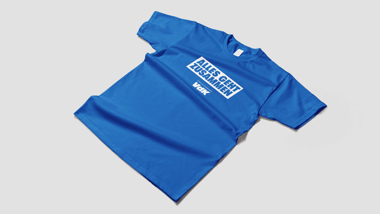 Blaues T-Shirt mit wei&szlig;em Studio Good-Logo auf der Vorderseite, flach auf einem neutralen Hintergrund ausgelegt.