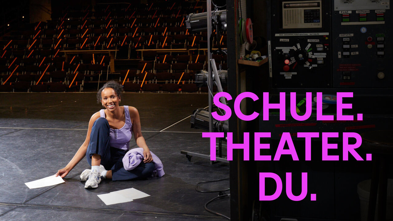 Eine Person in blauer Sportkleidung sitzt entspannt auf einem dunklen B&uuml;hnenboden, umgeben von Theaterrequisiten. Neben ihr leuchten die pinken Worte "SCHULE. THEATER. DU." vor einem industriellen Hintergrund.