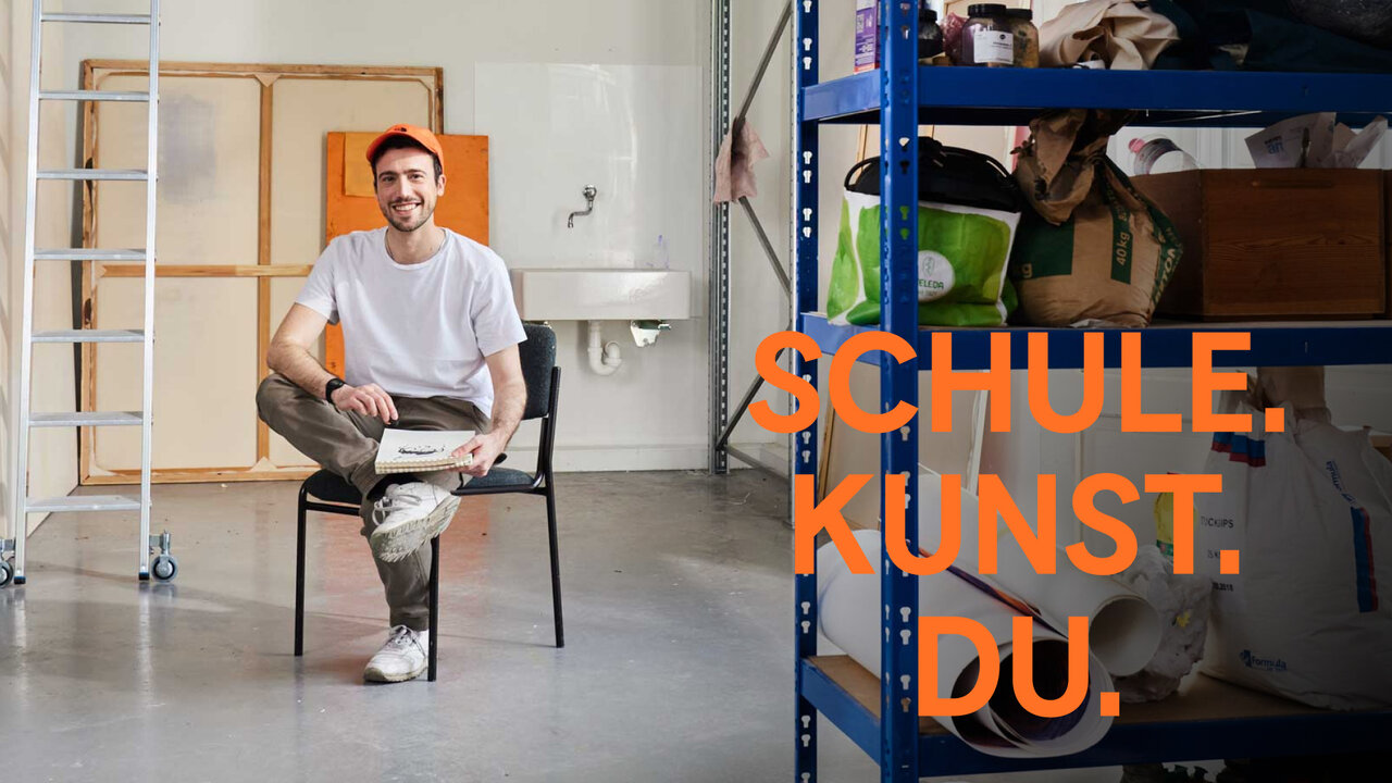 Ein l&auml;chelnder Mann in wei&szlig;em T-Shirt sitzt auf einem Stuhl in einem minimalistischen Raum mit Leiter und orangefarbenem Akzent. Daneben ein Regal mit verschiedenen Gegenst&auml;nden und ein orangefarbener Schriftzug "SCHULE. KUNST. DU." im Design einer Kampagne f&uuml;r die Universit&auml;t der K&uuml;nste Berlin.
