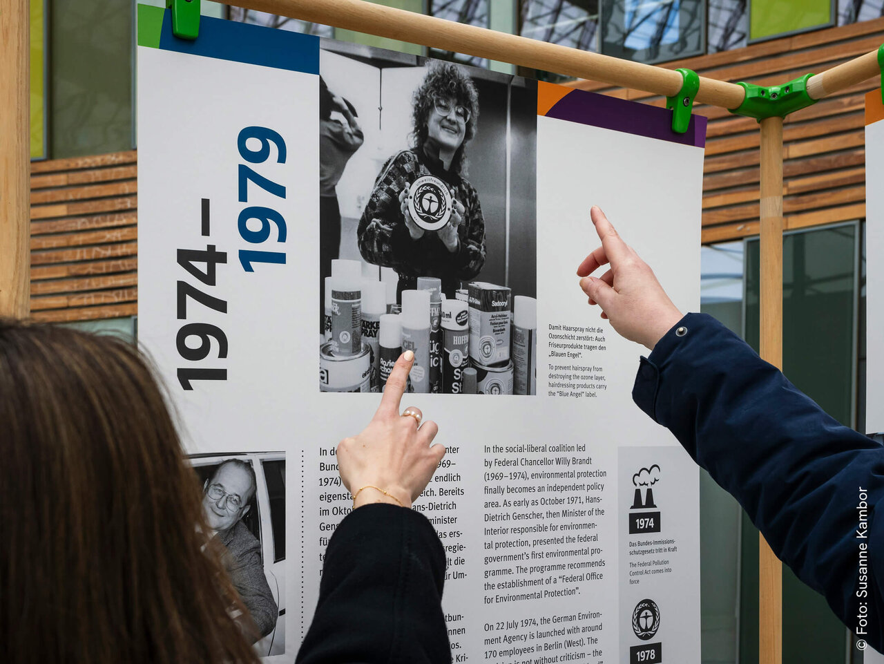 Zwei H&auml;nde zeigen auf ein schwarzwei&szlig;es Ausstellungsplakat mit historischem Foto und Jahreszahlen zwischen 1974 und 1979, das Teil einer zeitgeschichtlichen Dokumentation zu sein scheint.