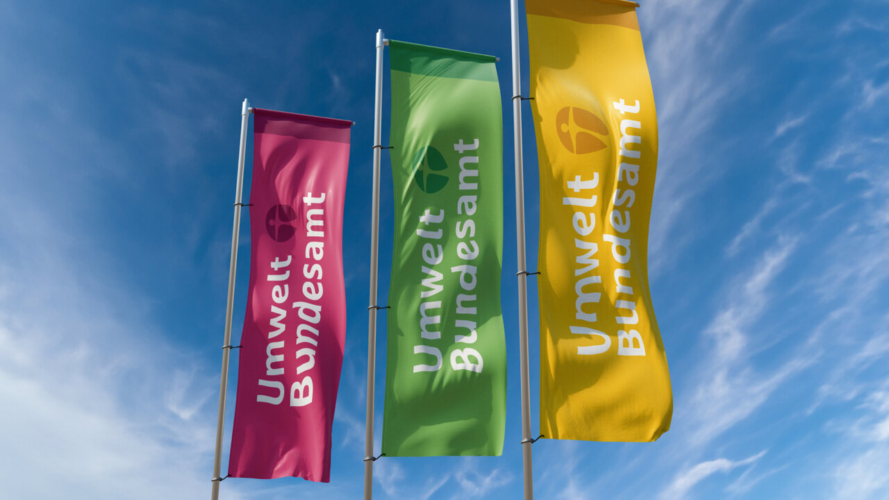 Drei Fahnen des Umweltbundesamtes in Rosa, Gr&uuml;n und Gelb vor blauem Himmel mit leichten Wolken, die das Corporate Design der Umweltbeh&ouml;rde repr&auml;sentieren.