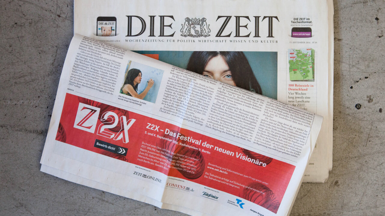 Zwei &uuml;bereinander liegende Zeitungen: Die Zeit und eine Beilage mit dem Logo Z2X, auf einem grauen Untergrund platziert. Die Zeitungen sind gefaltet, sodass Titel und Designelemente sichtbar sind.