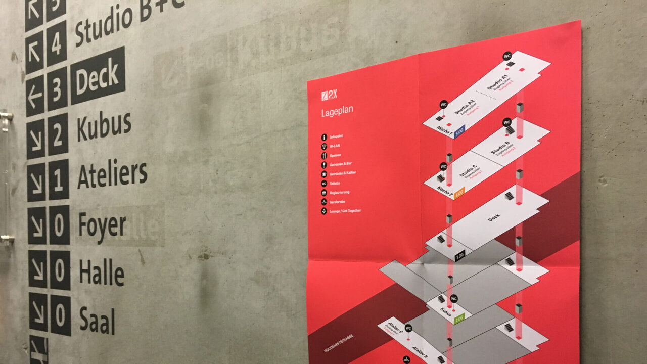 Rote Infografik mit isometrischer Darstellung eines mehrst&ouml;ckigen Geb&auml;udegrundriss-Plans neben einer Beschilderung mit Stockwerken und Bereichen wie Foyer, Halle und Saal in einem Industriegeb&auml;ude.