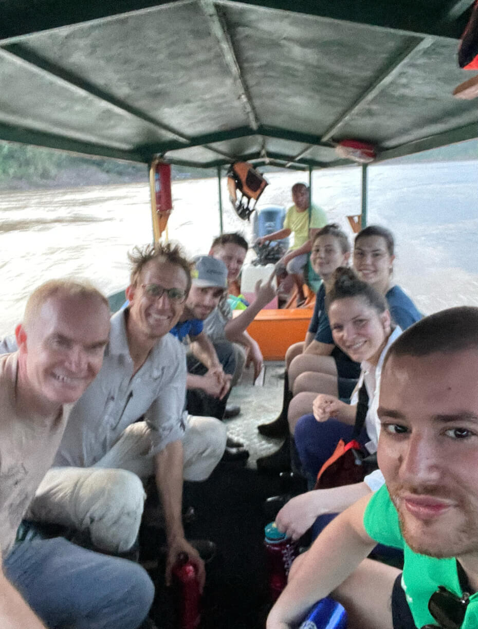 Gruppe von Menschen sitzt in einem &uuml;berdachten Boot. Mehrere Personen l&auml;cheln und blicken in verschiedene Richtungen. Die Sitzreihen sind eng und die Stimmung scheint locker und freundlich.
